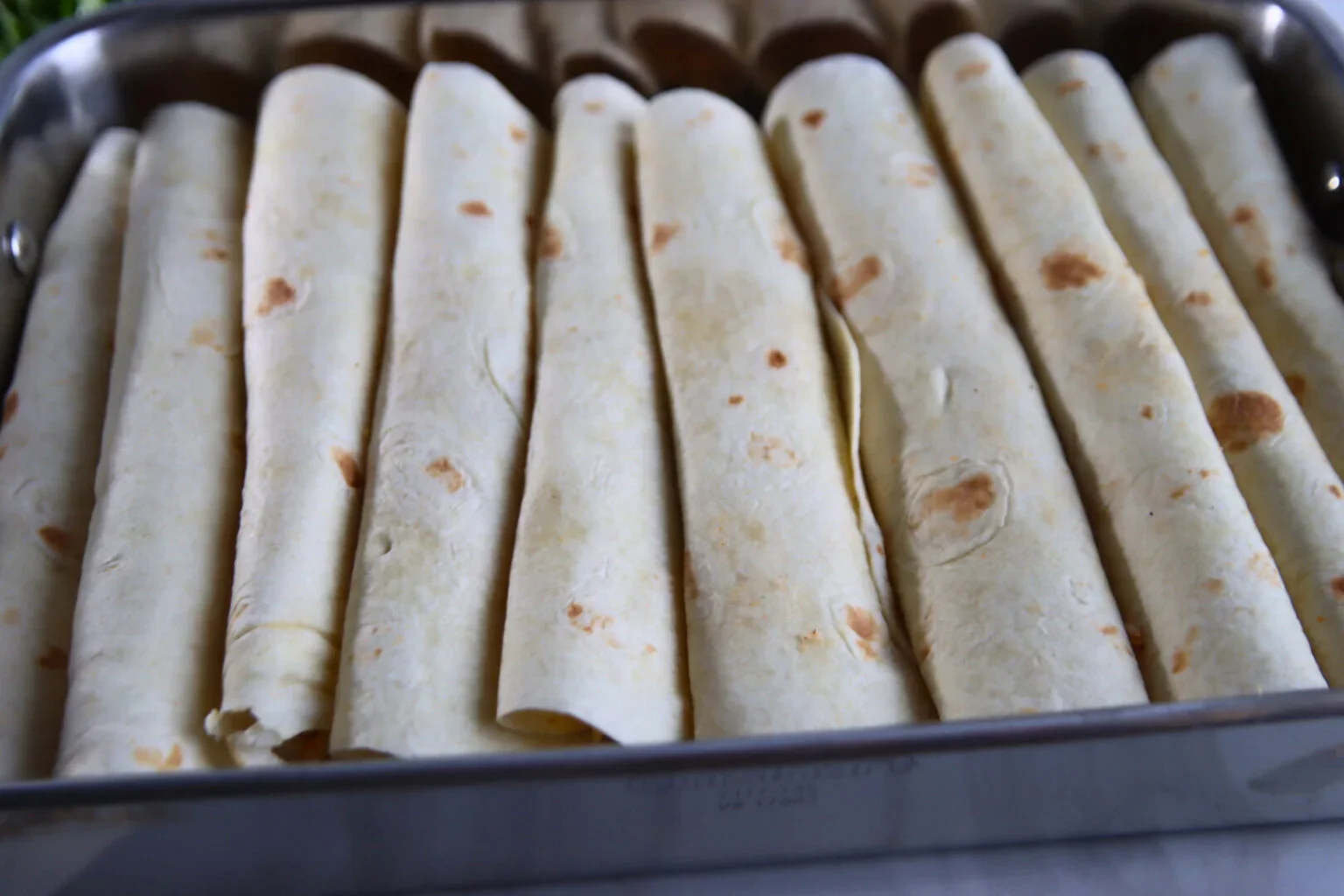 Eight rolled chicken enchiladas arranged in a rectangular baking pan.