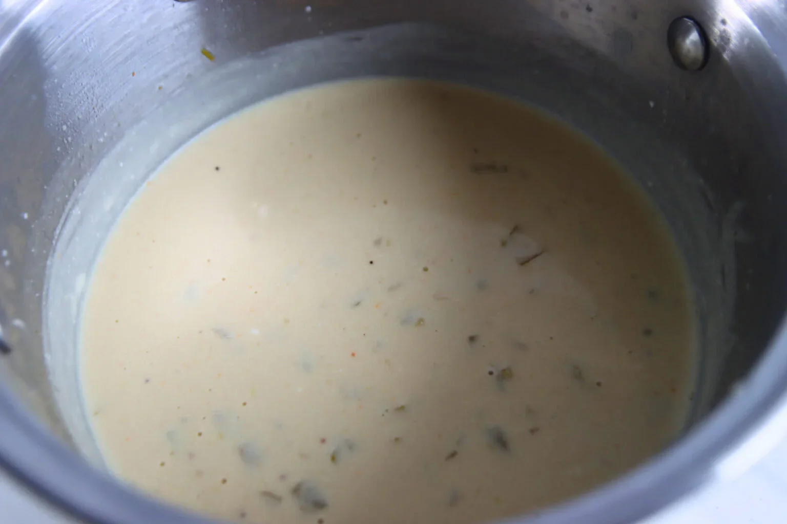 Creamy white enchilada sauce with green chiles simmering in a saucepan.