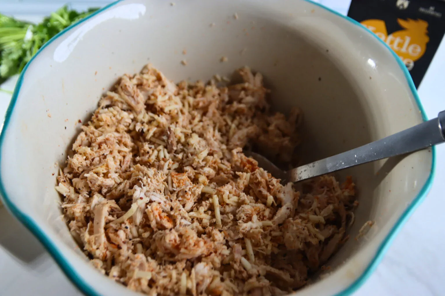 Shredded chicken mixed with Monterey Jack cheese and Dia de la Fajita seasoning in a bowl.