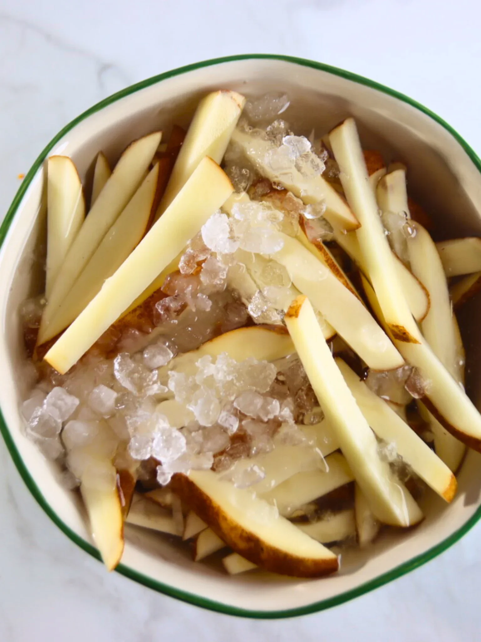 Fresh-cut russet potato fries soaking in ice water in a bowl.