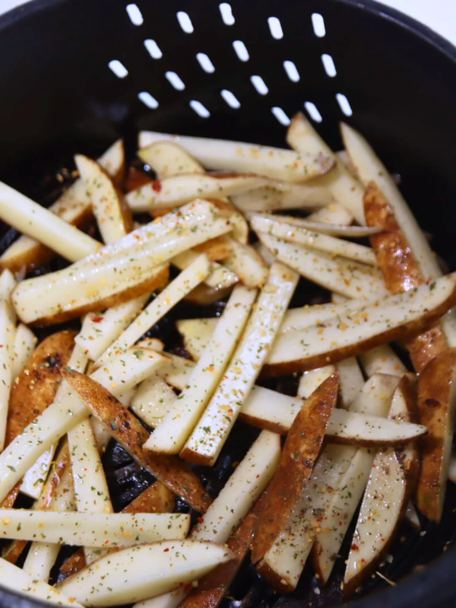 Raw potato fries coated with oil and seasonings inside an air fryer basket.