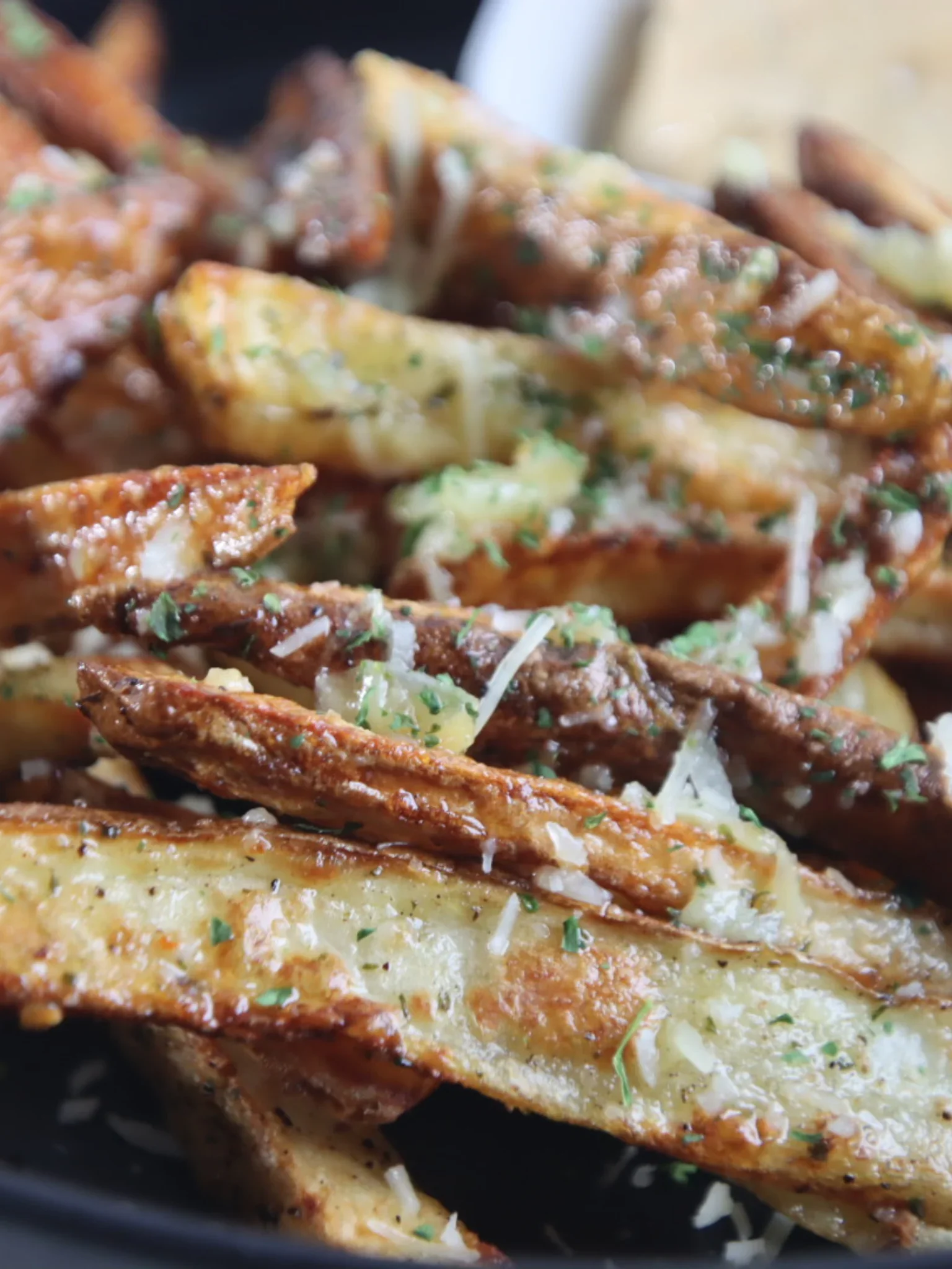 Close-up of golden garlic Parmesan fries garnished with shredded cheese and parsley.